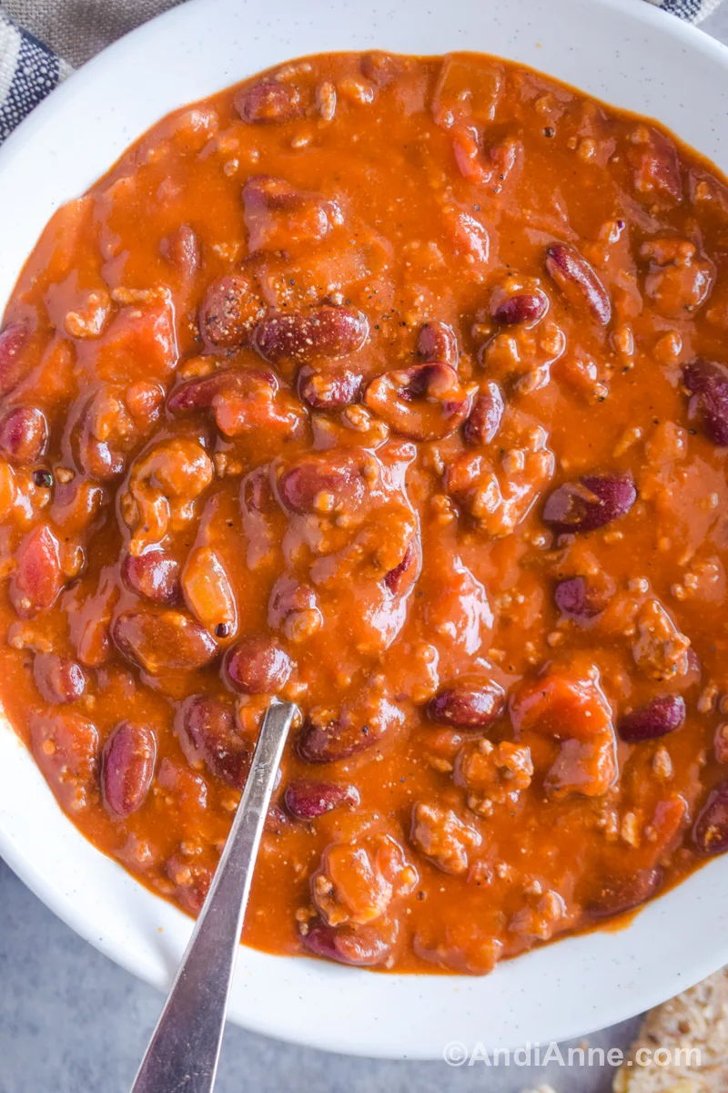 Close up of homemade chili in a white bowl with a spoon.