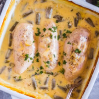 Cream of chicken soup with chicken breasts and green beans in a square white baking dish.