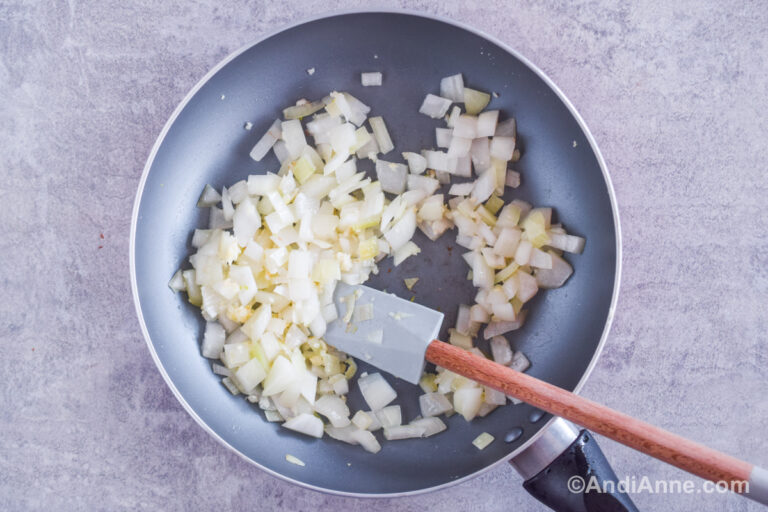 A frying pan with chopped onion and a spatula.