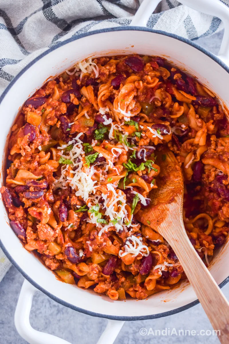 A white pot with spiral noodles, beans, ground pork in a tomato sauce and sprinkled with mozzarella cheese.