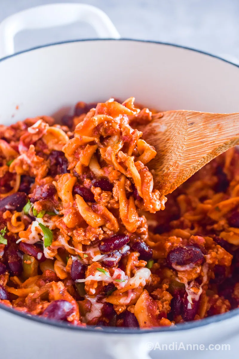 A wood spoon scooping the recipe including spiral noodles, kidney beans and ground pork in a tomato sauce mixture.