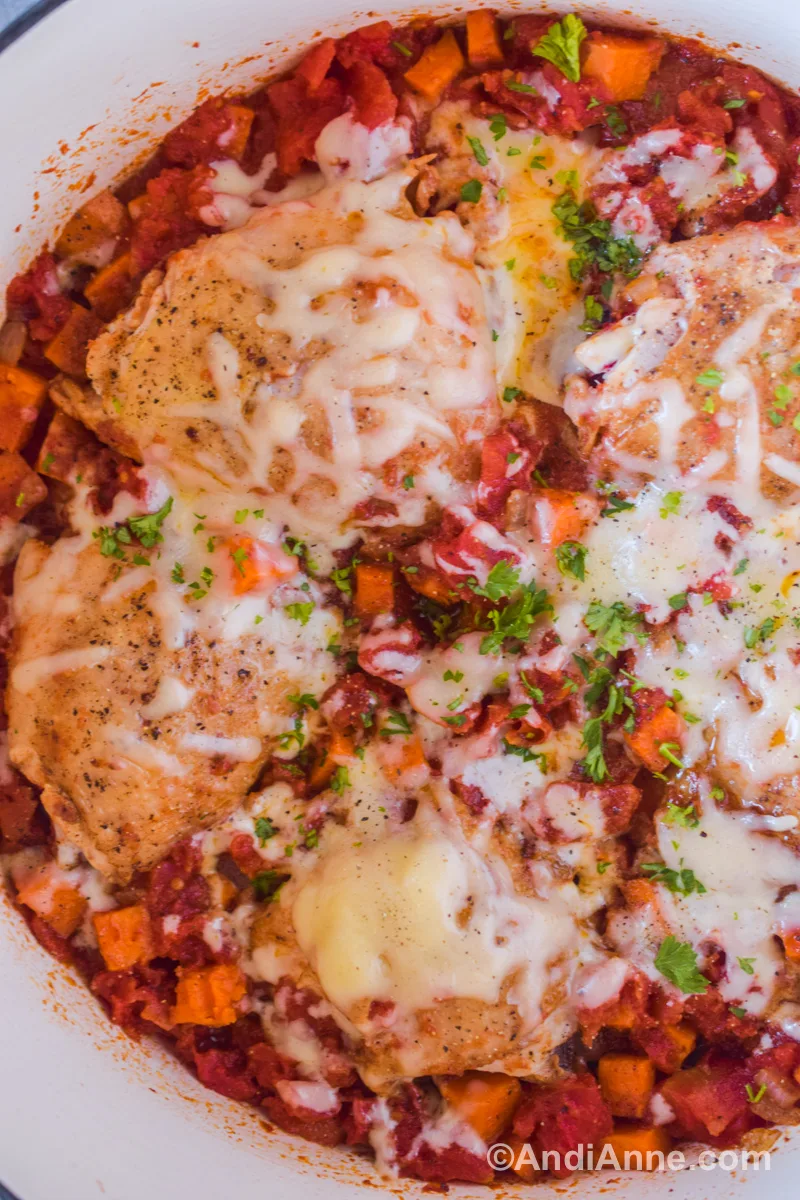 Close up of melted cheese on top of cooked chicken thighs, diced tomatoes and chopped sweet potatoes.