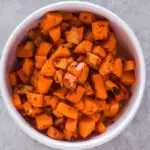 A white bowl of cooked chopped sweet potatoes.
