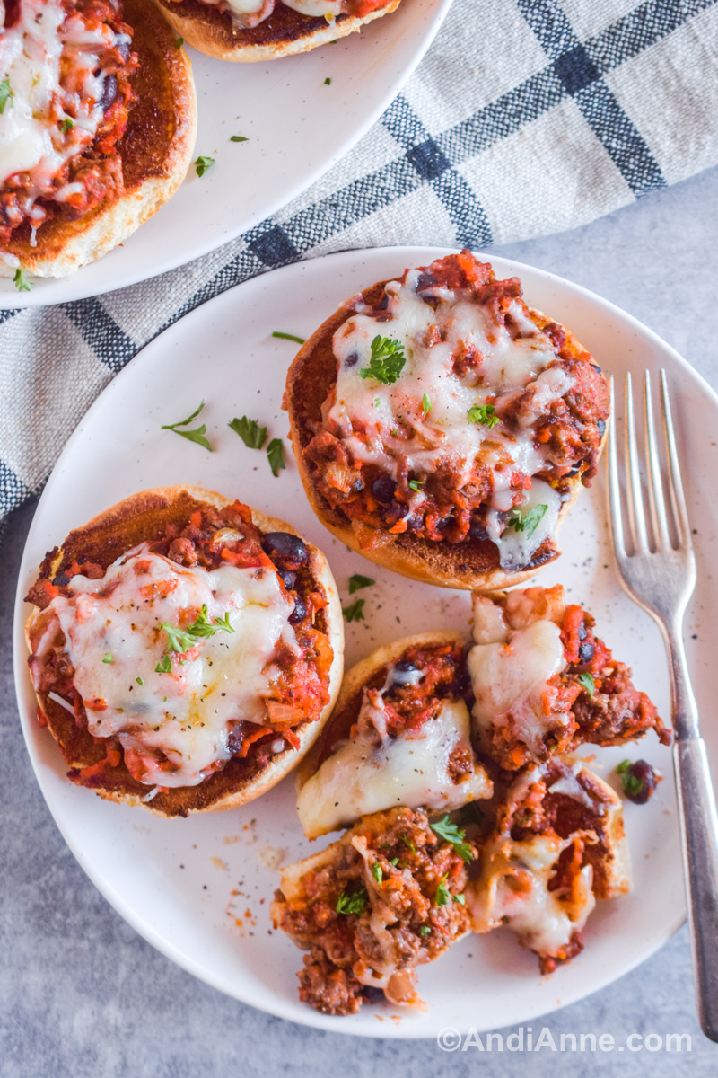 Three pizza sloppy joes on a plate. Once sliced into four pieces with a fork beside.