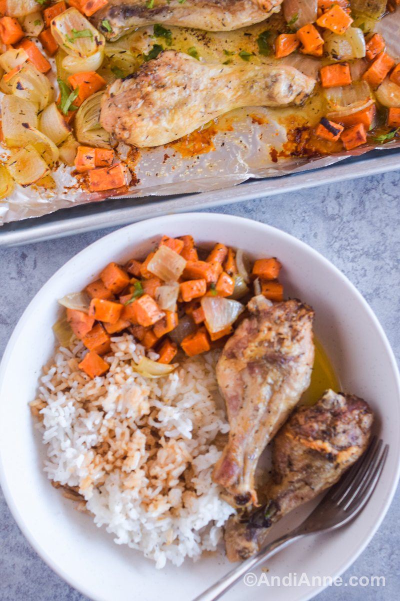 A white plate with chicken legs, rice and chopped sweet potato and a fork. 