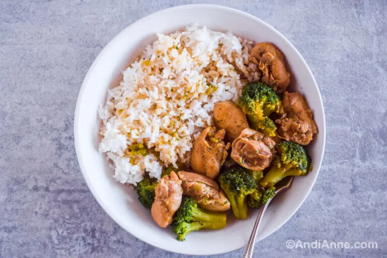 A white plate with cooked rice and chicken thighs with broccoli.
