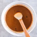 A bowl of brown sauce with a small spoon.