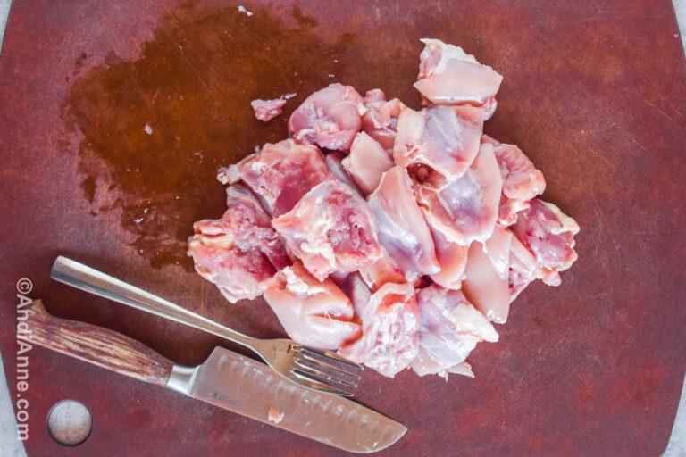 Chopped raw chicken on a cutting board with a knife and a fork.