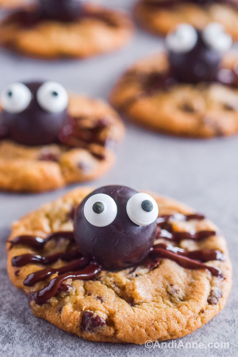 Close up of a chocolate chip cookie with a round chocolate with candy eyeballs and chocolate stripes to look like a spider.