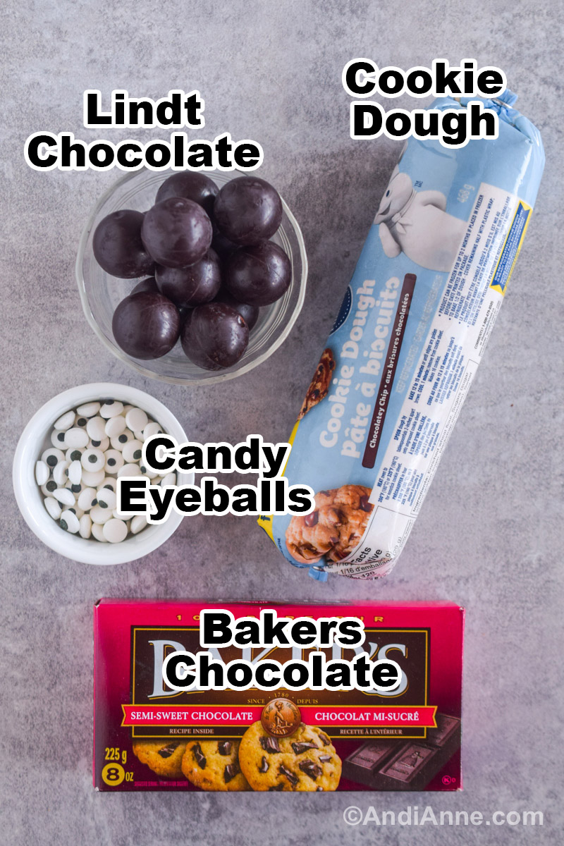 Recipe ingredients on the counter including a roll of cookie dough, chocolate balls, candy eyeballs and bakers chocolate.