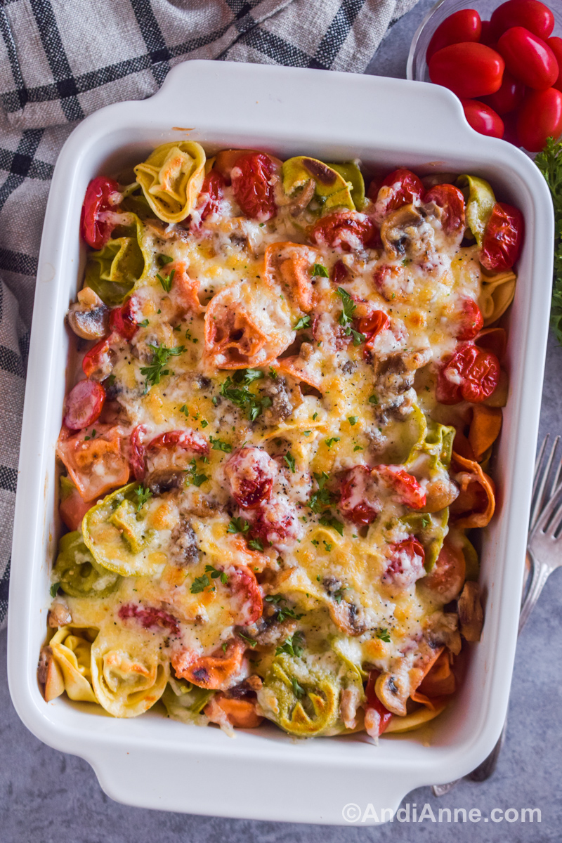 A white casserole dish with baked tortellini pasta and mushrooms covered in cheese. 