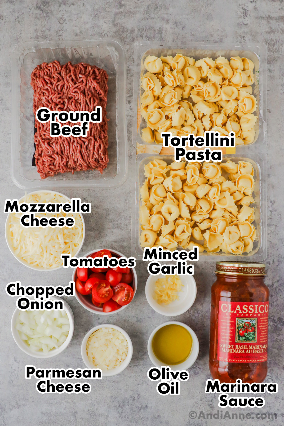 Recipe ingredients including raw ground beef, 2 packs of tortellini pasta, bowls of mozzarella cheese, sliced tomatoes, chopped onion, parmesan cheese, minced garlic and jar of marinara.