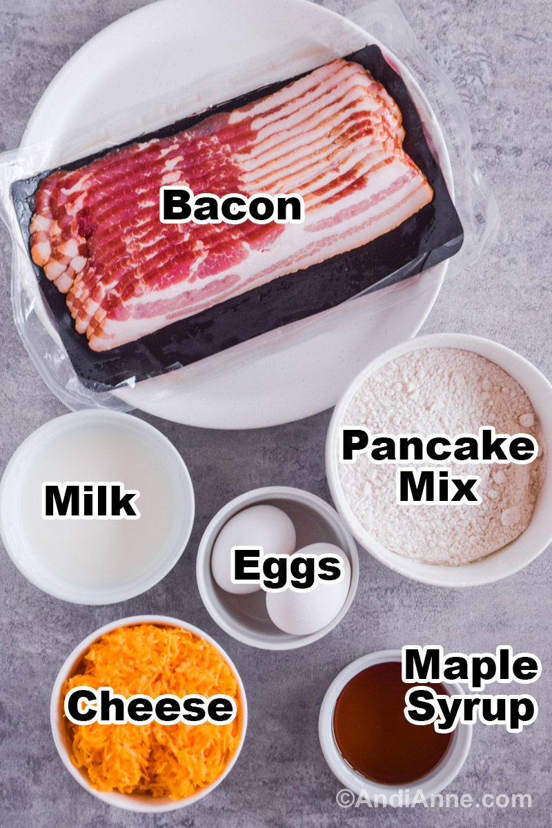 Recipe ingredients on the counter including raw bacon, bowls of milk, pancake mix, eggs, shredded cheese and maple syrup.