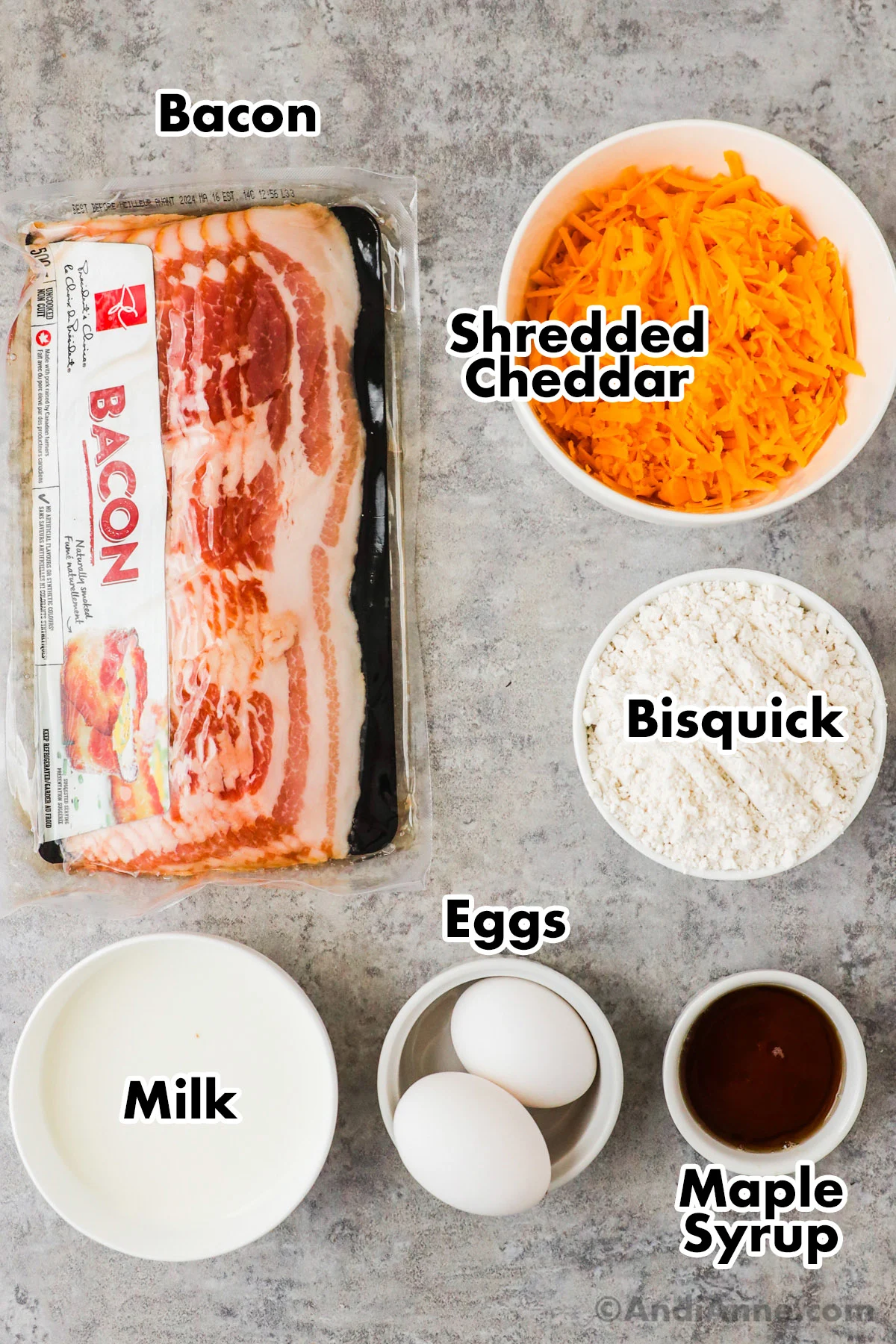 Recipe ingredients including a package of bacon, bowl of shredded cheese, bowl of bisquick mix, bowl of milk, 2 eggs and maple syrup.