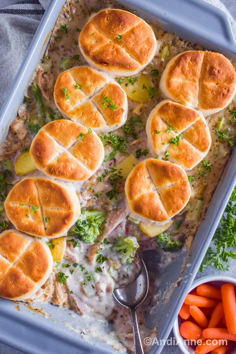 Close up of chicken pot pie recipe with a spoon inside the casserole dish and bowl of carrots nearby.