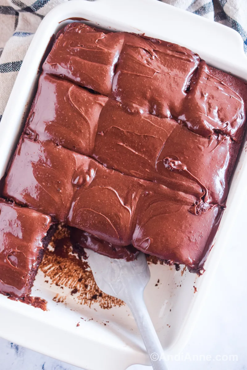 Looking down at a white dish with sliced chocolate mayonnaise cake inside and a spatula.