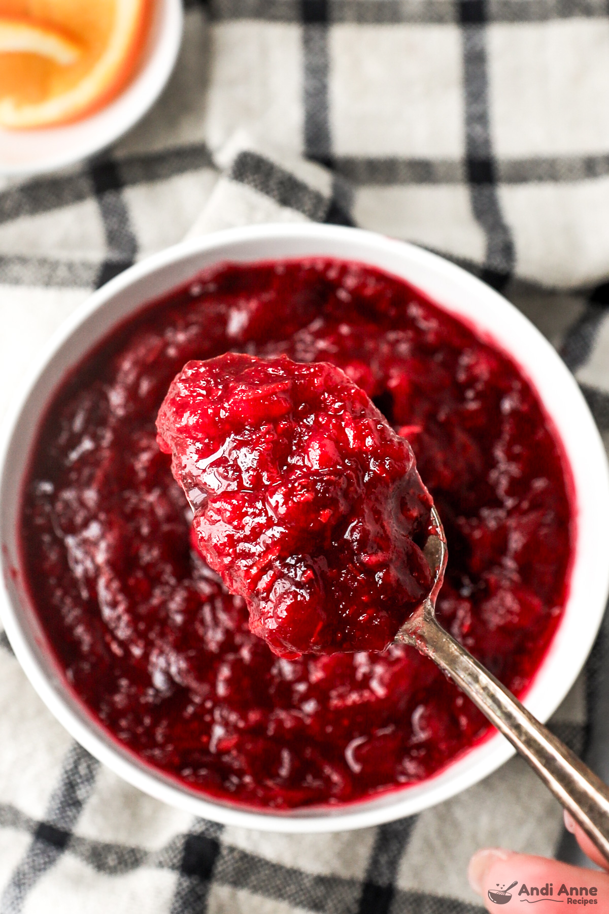 Close up of a spoon scooping cranberry sauce with a bowl of the sauce in the background