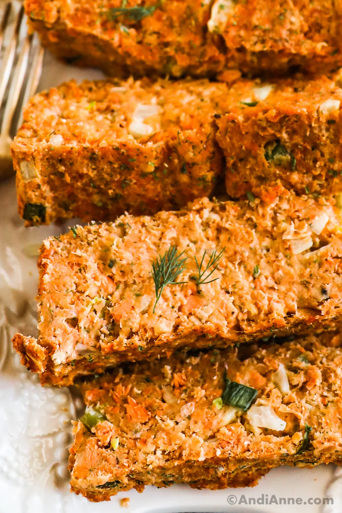 Close up of salmon loaf slices and a fork on a white plate. 