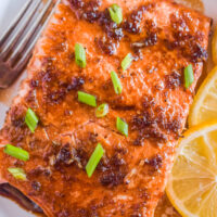 Soy sauce brown sugar salmon on a plate with lemon slices and chopped green onion.