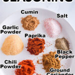 Piles of spices on a plate including cumin, garlic powder, salt, paprika, chili powder, and ground coriander. This are ingredients to make chicken taco seasoning.