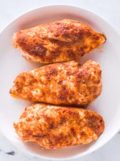 Closeup of seasoned chicken breasts on a white plate