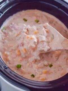 cowboy crack dip in a slow cooker with a wooden spoon.