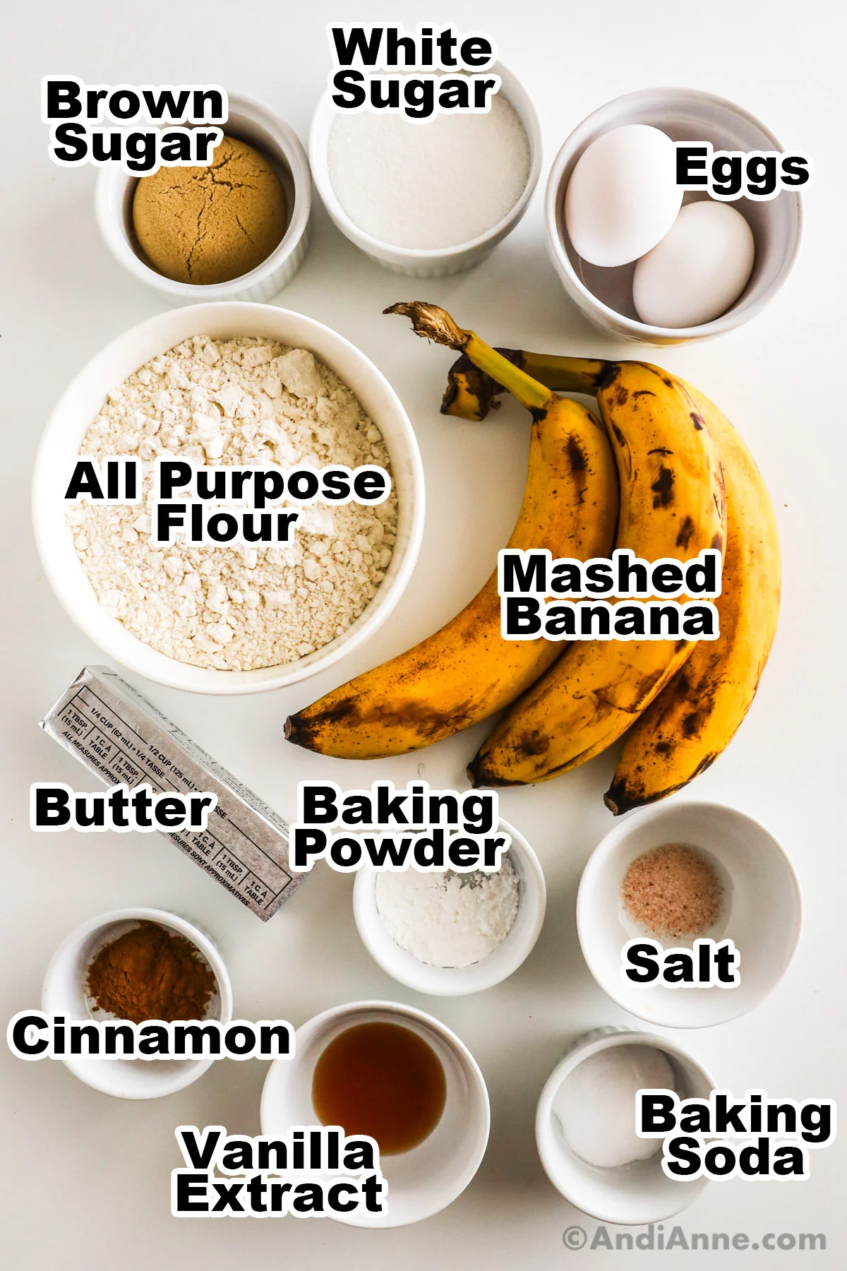 Recipe ingredients on the counter including bowls of brown sugar, white sugar, eggs, flour, ripe bananas, butter, baking powder, salt, cinnamon and baking soda.