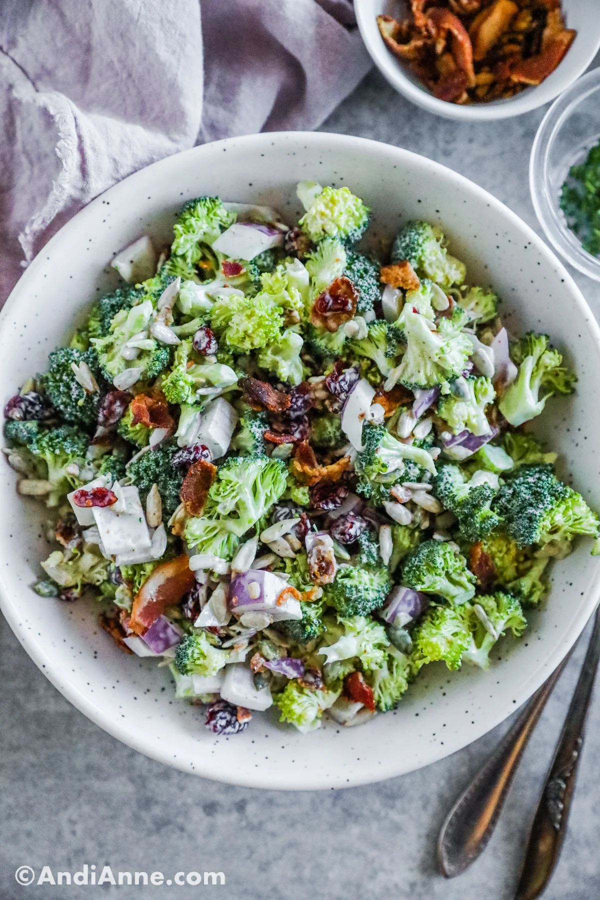 Broccoli crunch salad recipe in a white serving bowl with cutlery beside it. 