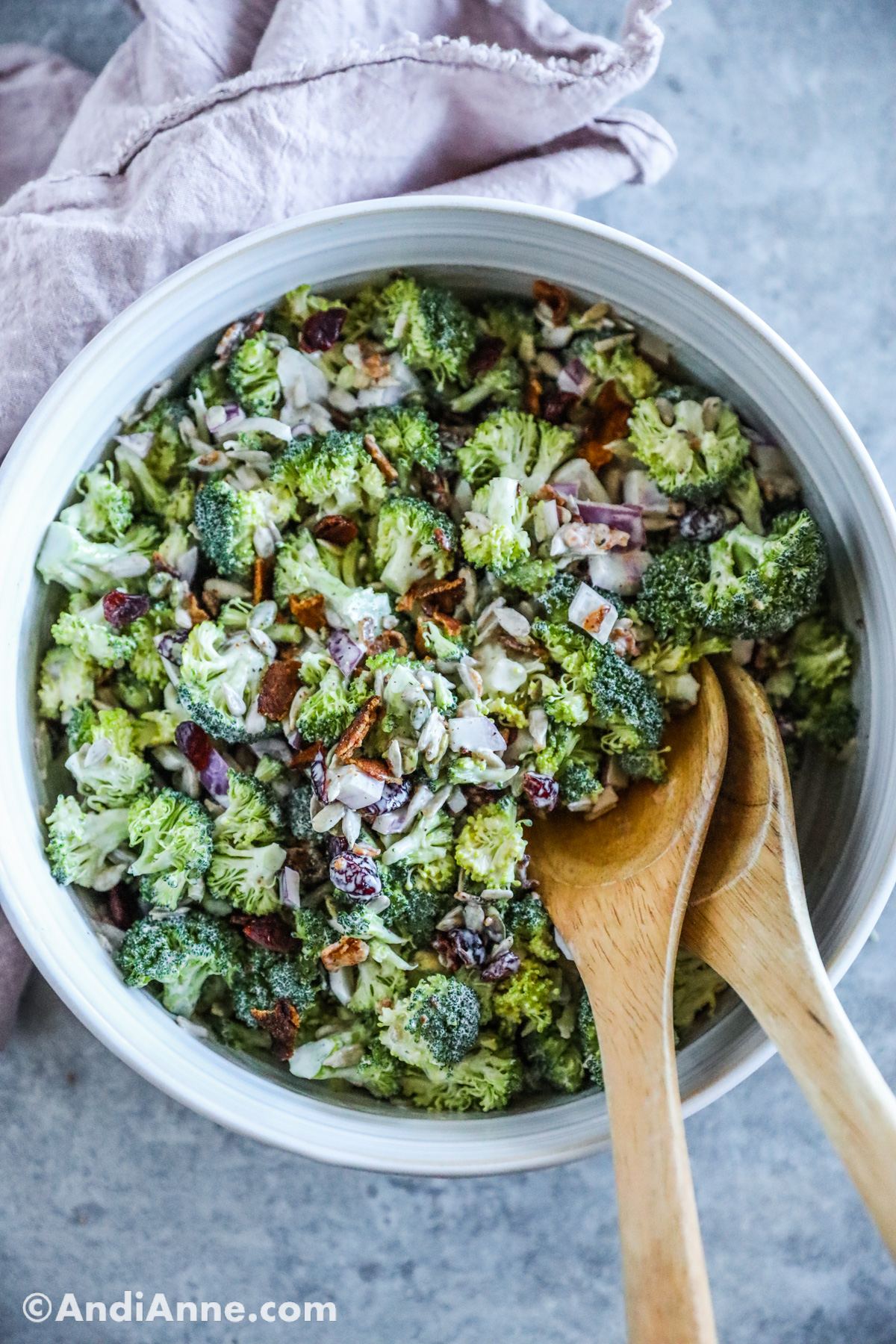 Looking down at creamy broccoli crunch salad in a white bowl with two wood salad spoons.
