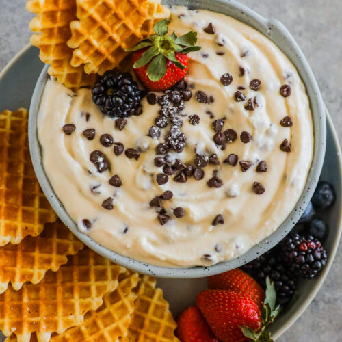 Cannoli dip in a bowl surrounded with waffle cookies, strawberries and blackberries.