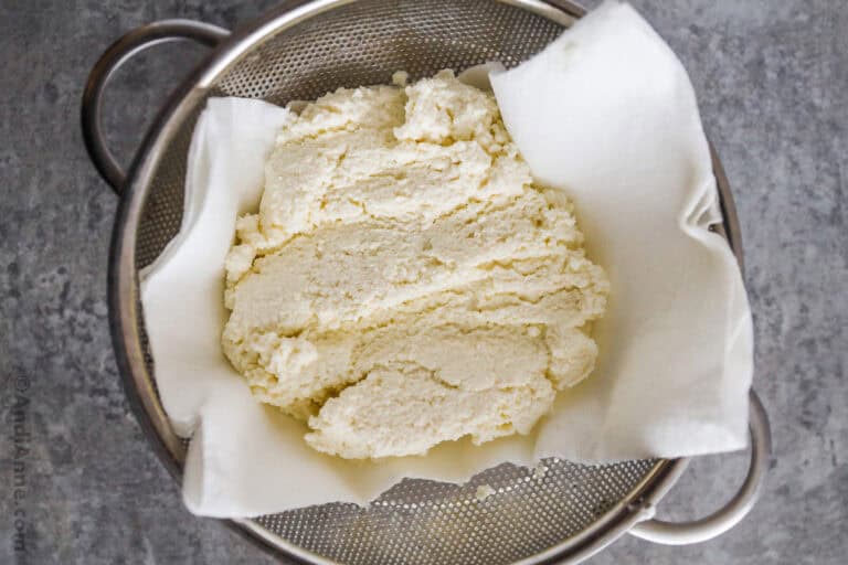 A strainer with paper towel and ricotta cheese on top.