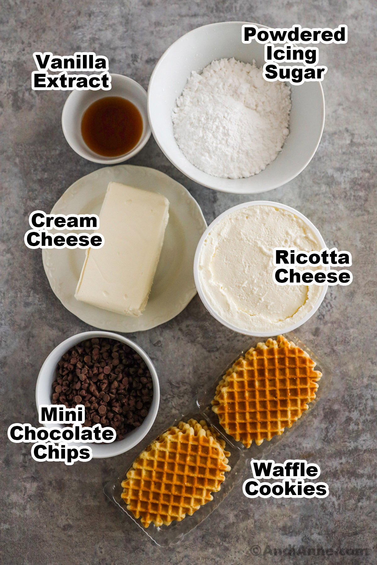 Recipe ingredients on the counter including bowls of vanilla extract, confectioners sugar, cream cheese, ricotta cheese, mini chocolate chips and butter waffle cookies.