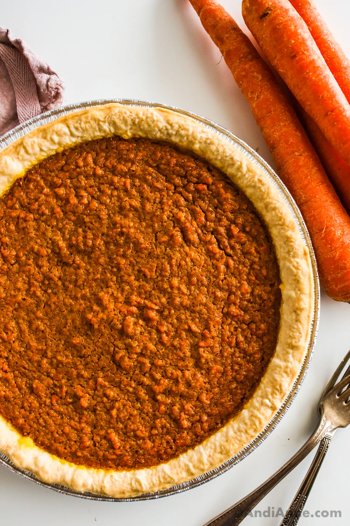 Close up of a carrot pie with forks and carrots beside it.