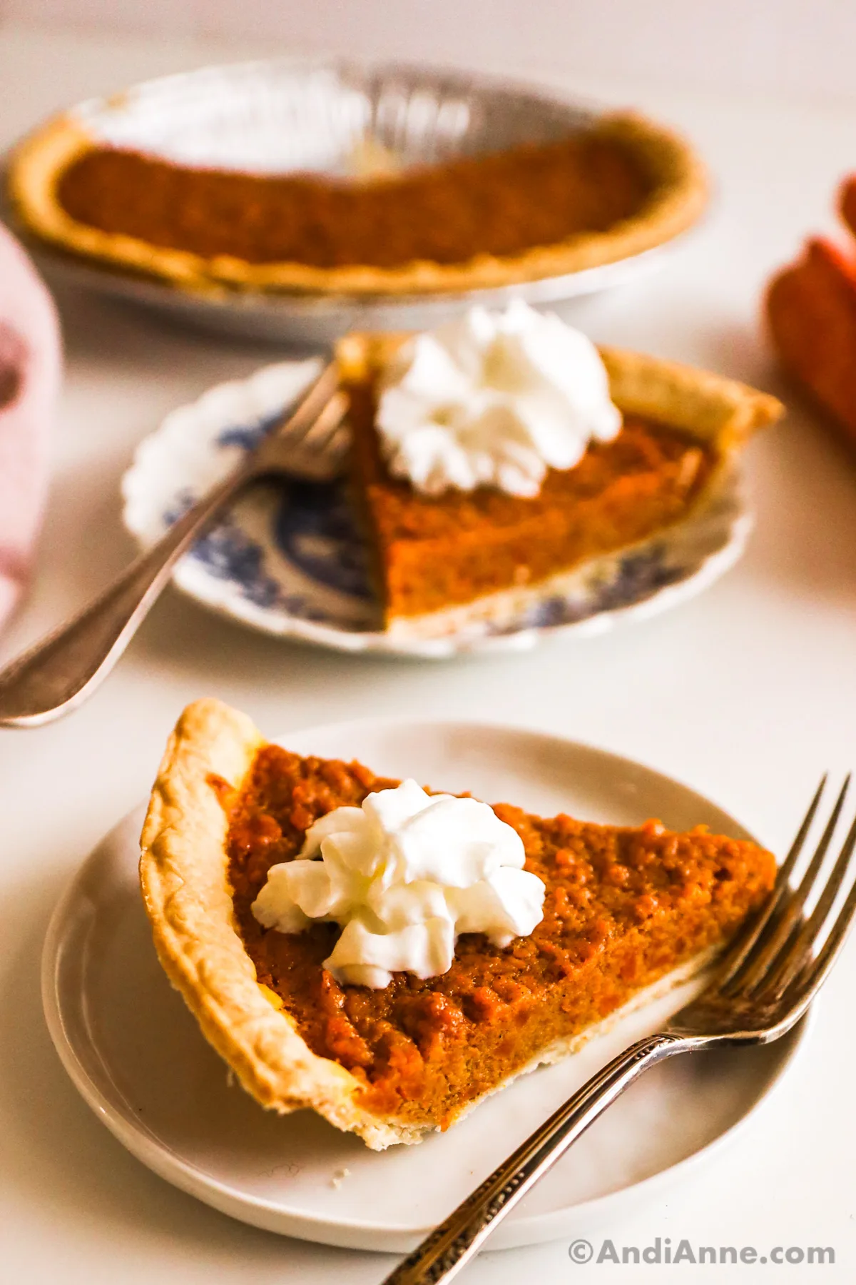 Two slices of carrot pie topped with whipped cream, on plates with forks.