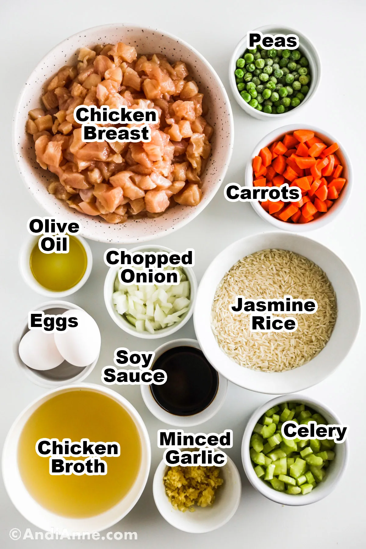 Recipe ingredients in bowls including chopped raw chicken, frozen peas, chopped carrots, olive oil, onion, jasmine rice, eggs, soy sauce, chicken broth, garlic and celery.