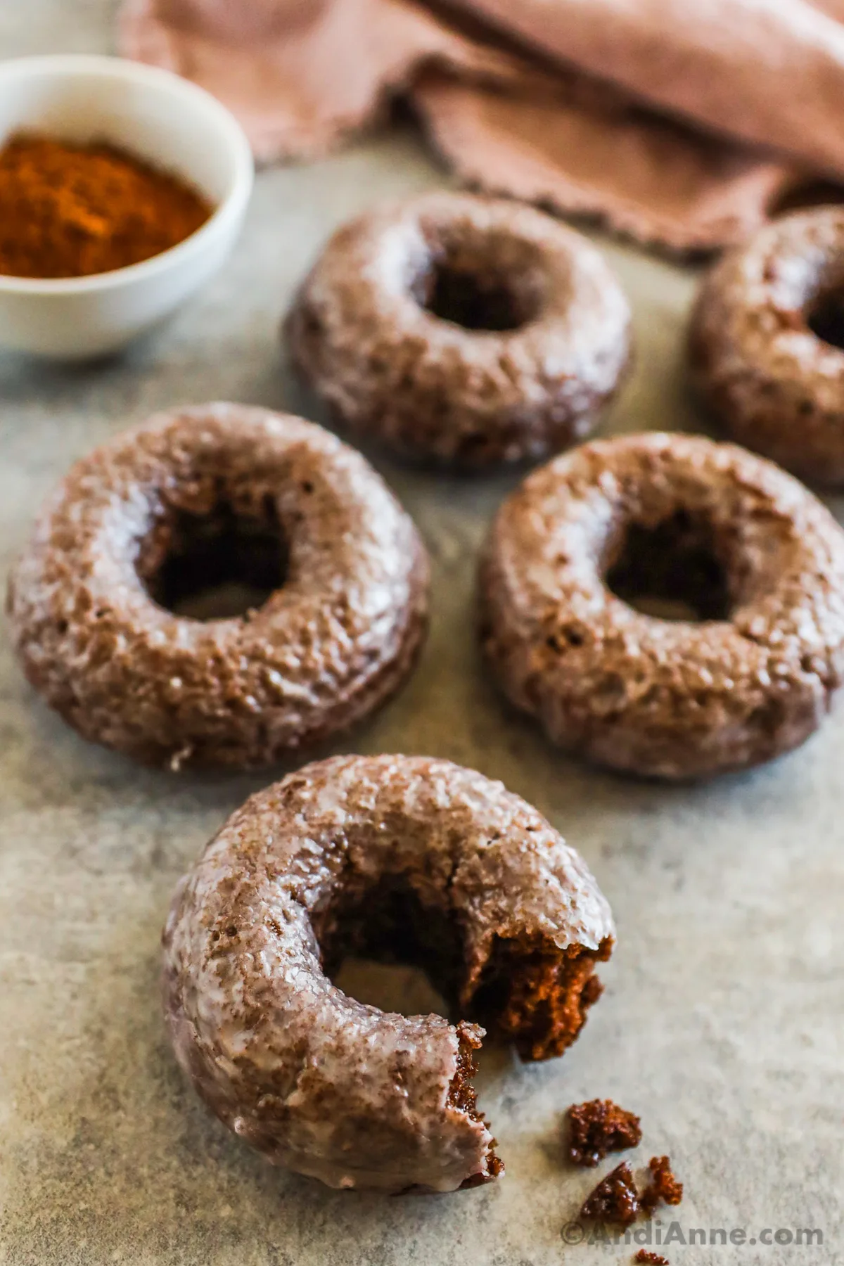 Close up of a bite taken out of a chocolate glazed donut with several donuts behind it.