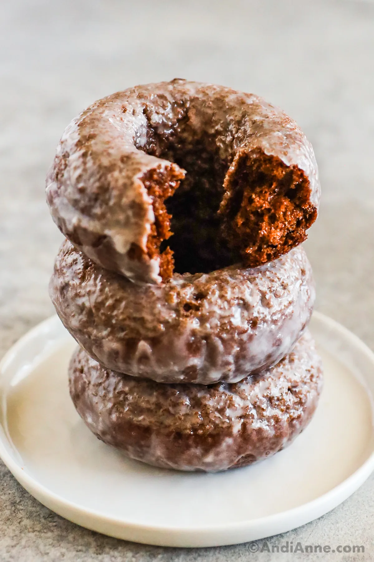 A stack of three donuts, the top one with a bite taken out.