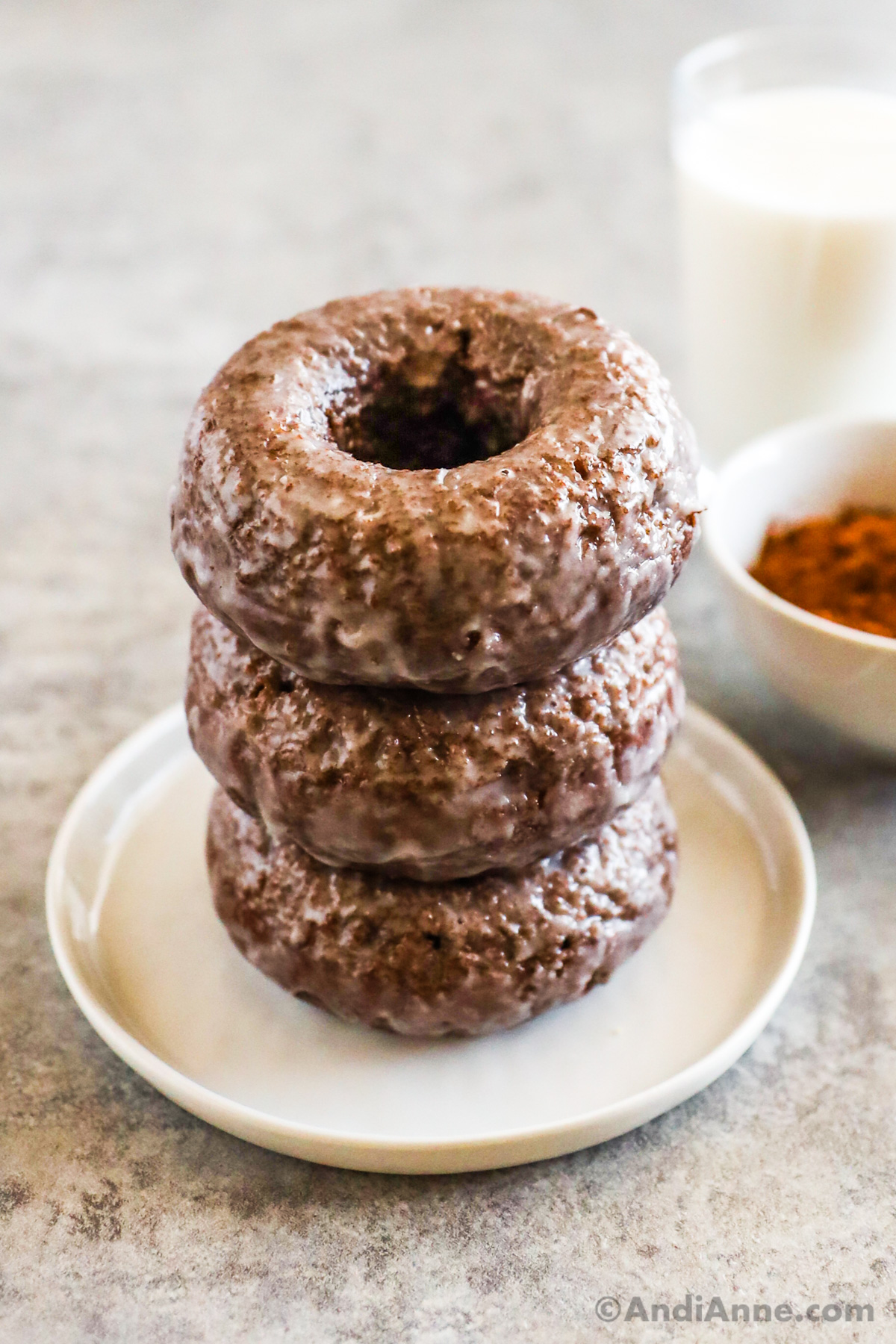 A stack of chocolate glazed donuts on a plate.