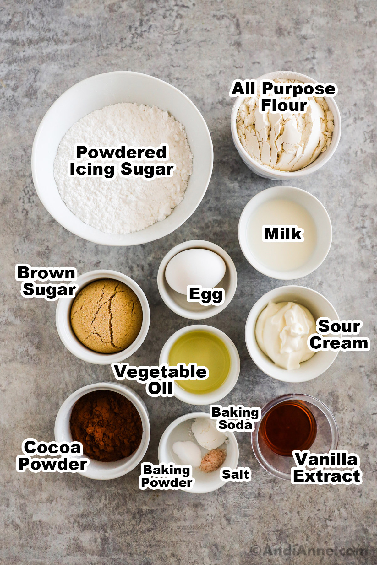 Ingredients on the counter in bowls including flour, milk, egg, brown sugar, vegetable oil, sour cream, cocoa powder, baking powder, vanilla extract.