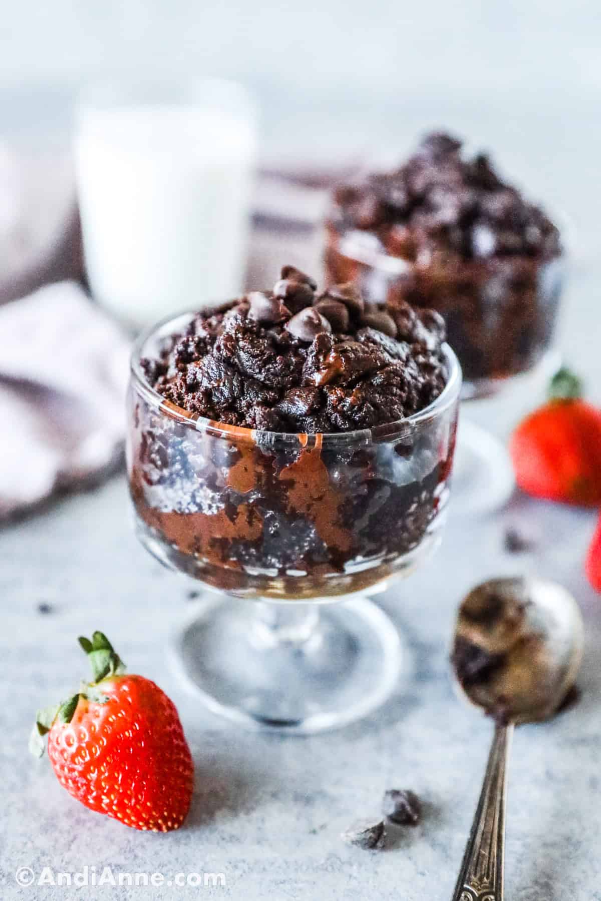 Two glass dishes with dessert, a spoon and strawberries on the table.