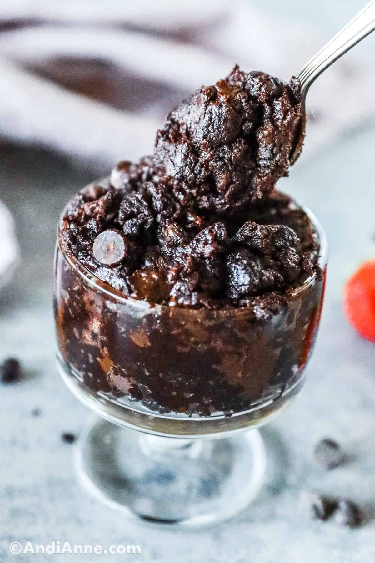 Close up of a spoon holding the brownie batter overtop of glass dish with the dessert.