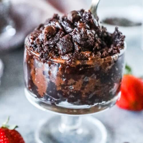 A glass cup of edible brownie batter with a spoon.