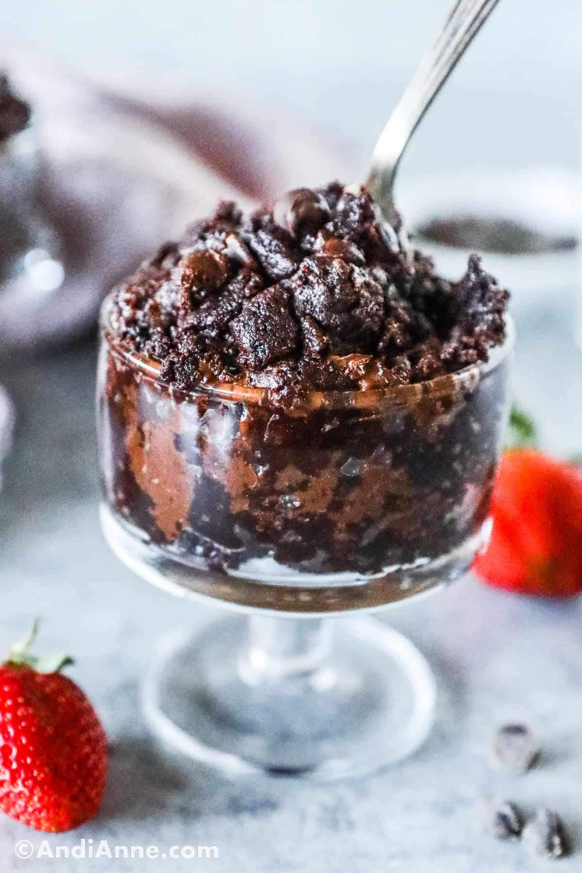 A glass cup of edible brownie batter with a spoon.