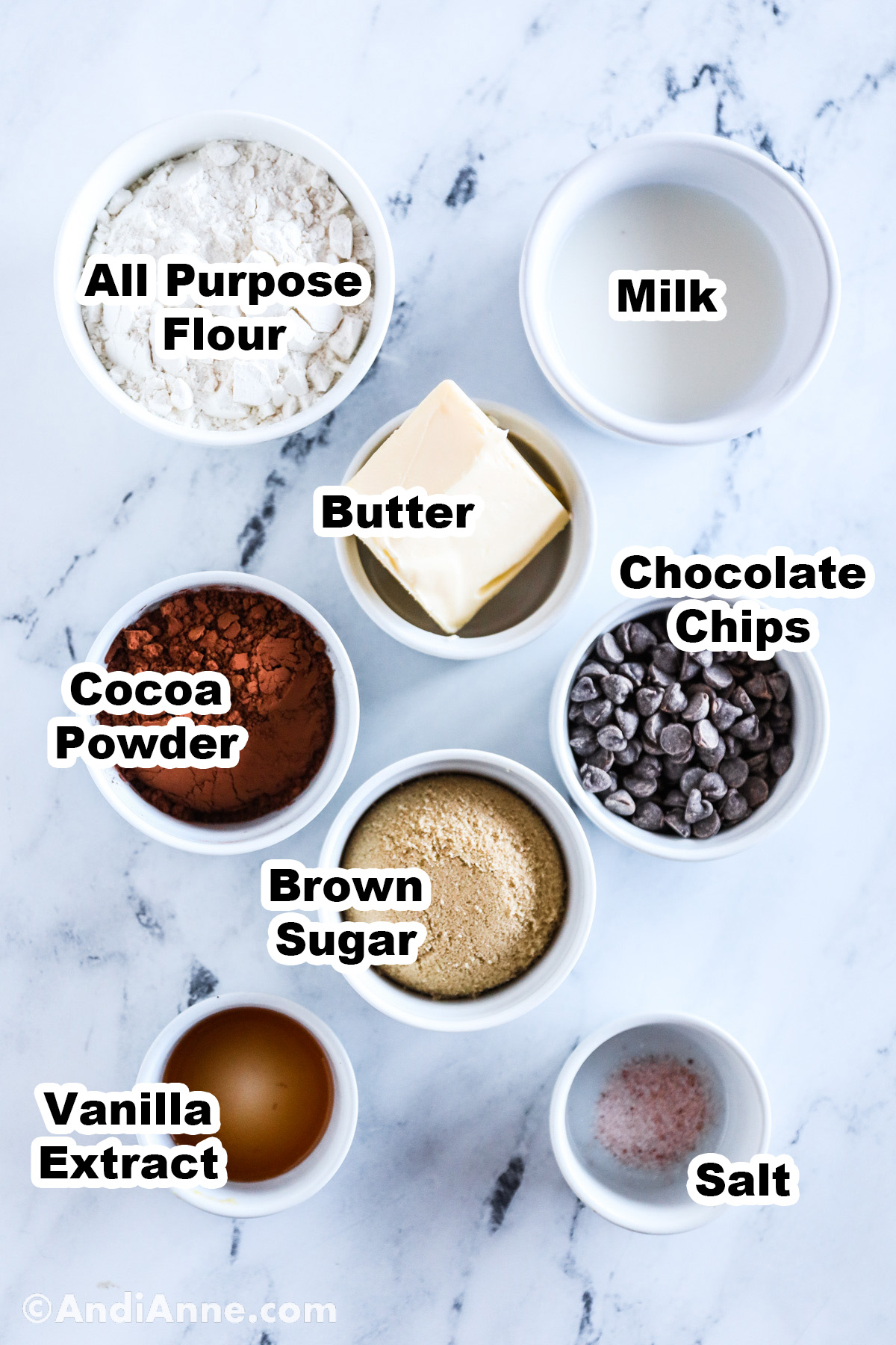 Recipe ingredients on the counter including bowls of flour, milk, butter, cocoa powder, brown sugar, chocolate chips, vanilla extract and salt.