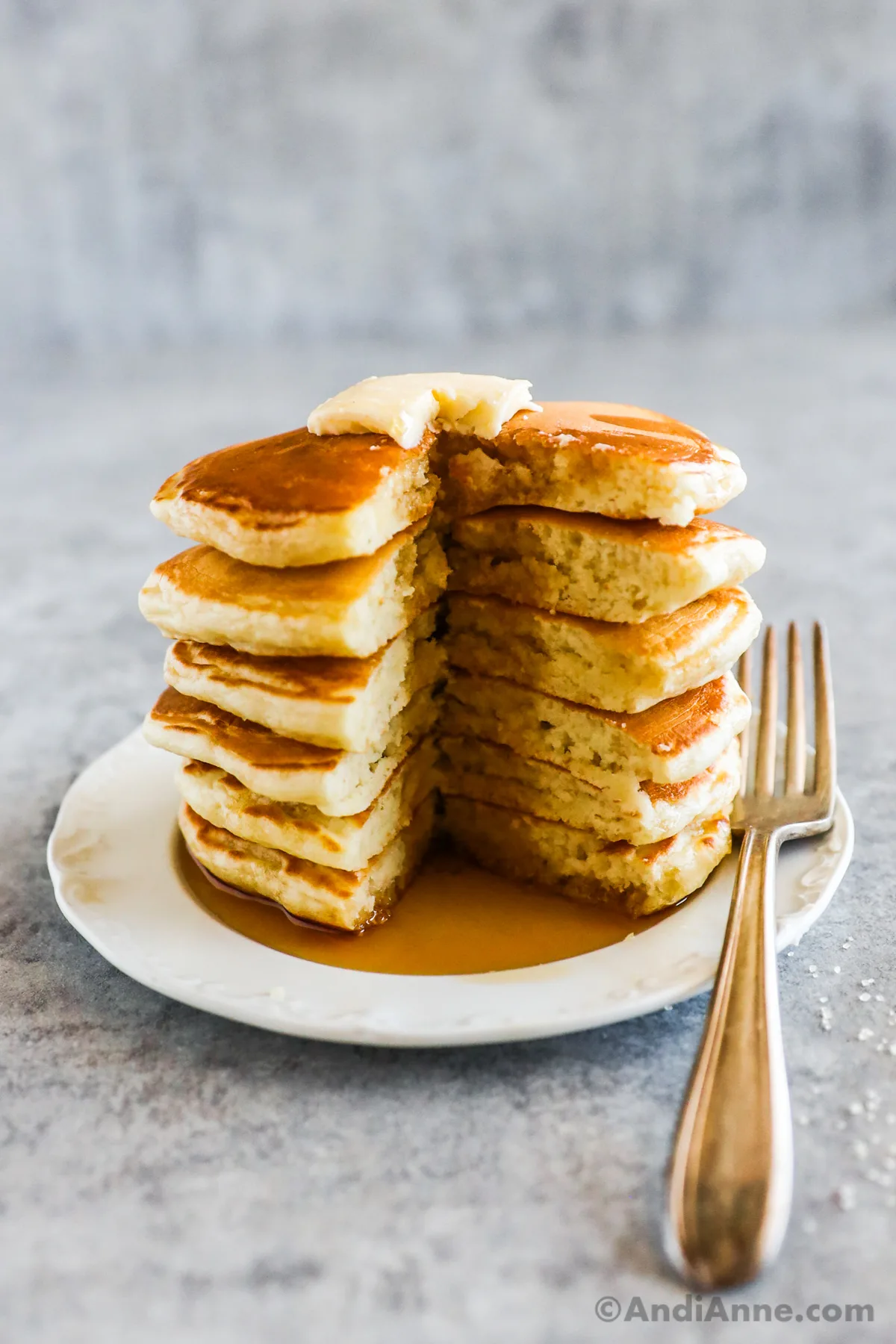 A stack of pancakes with butter and maple syrup. A triangle shaped slice is cut out and a fork beside on plate.