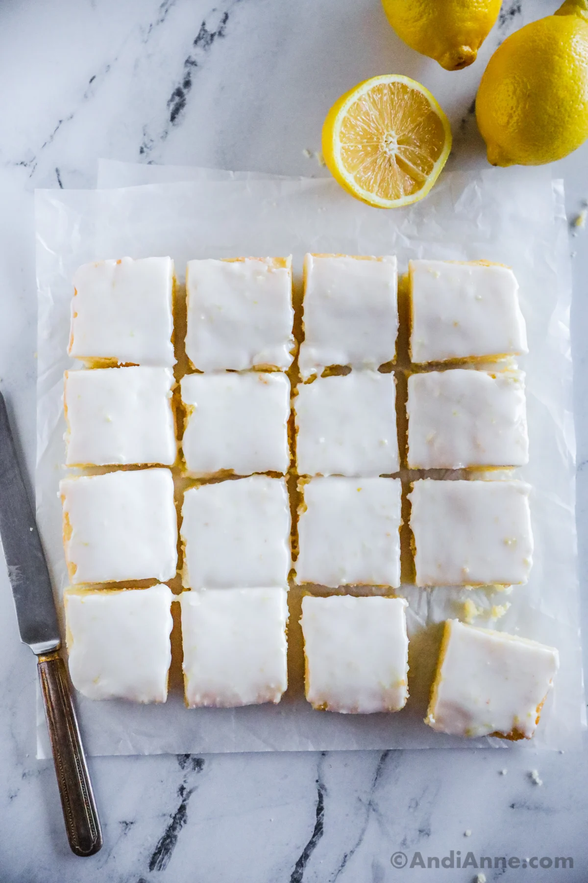 Lemon brownies with white glaze cut into squares on top of parchment paper.