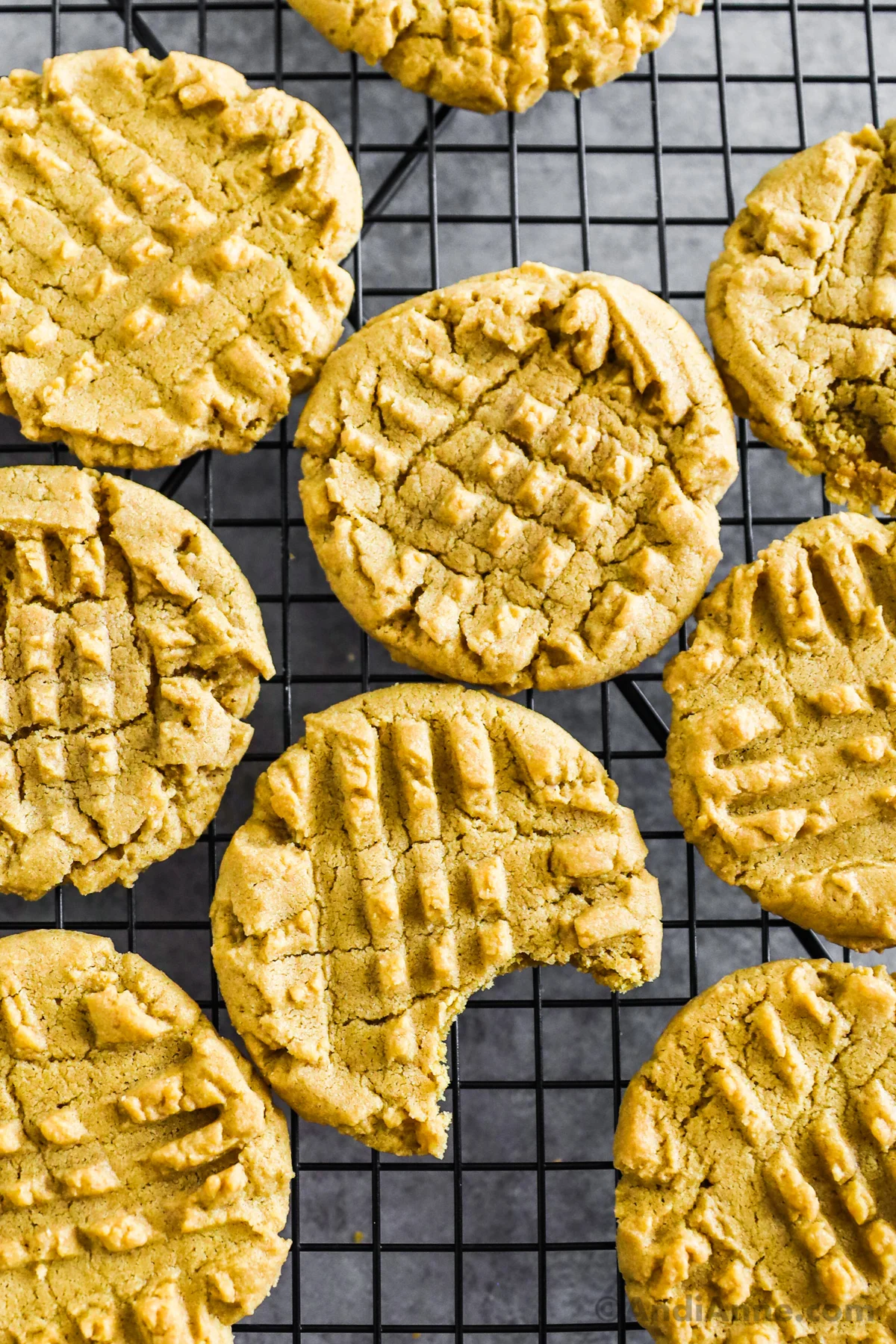 peanut butter cookies on a cooling rack, one with a bite taken out of.
