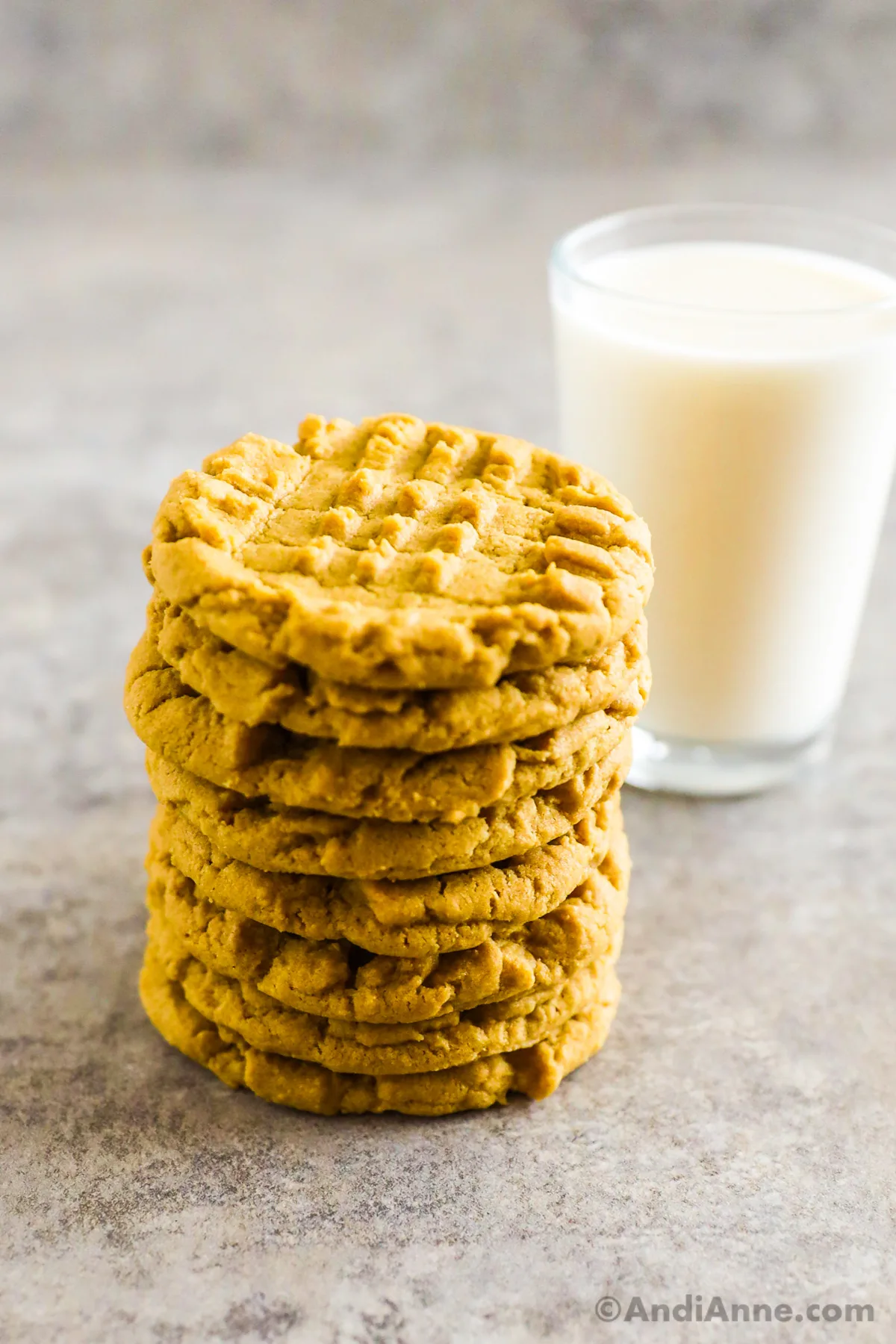 A stack of peanut butter cookies on top of each other with a glass of milk behind it. 