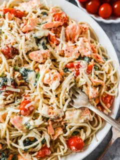 A bowl of creamy pasta with salmon, tomatoes and spinach