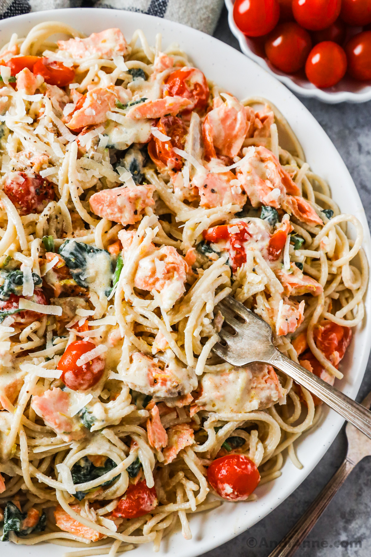 Close up of a fork in creamy pasta with salmon chunks, cherry tomatoes and spinach